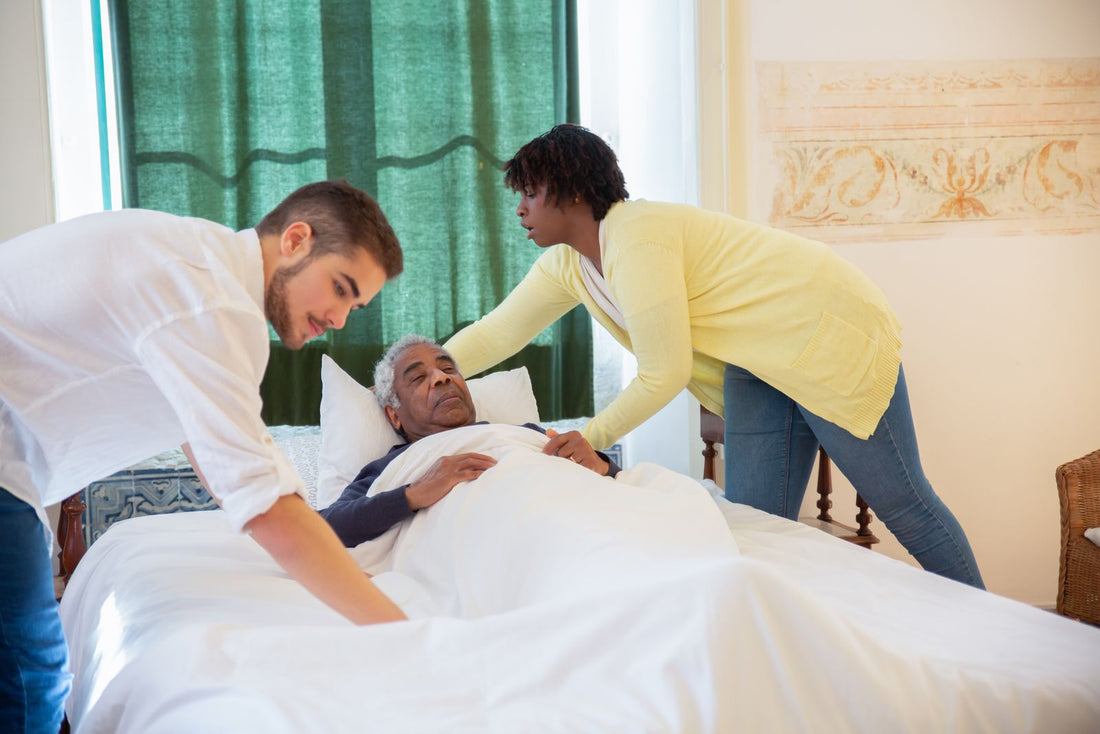 Two caregivers helping an older man get comfortable in bed for the night