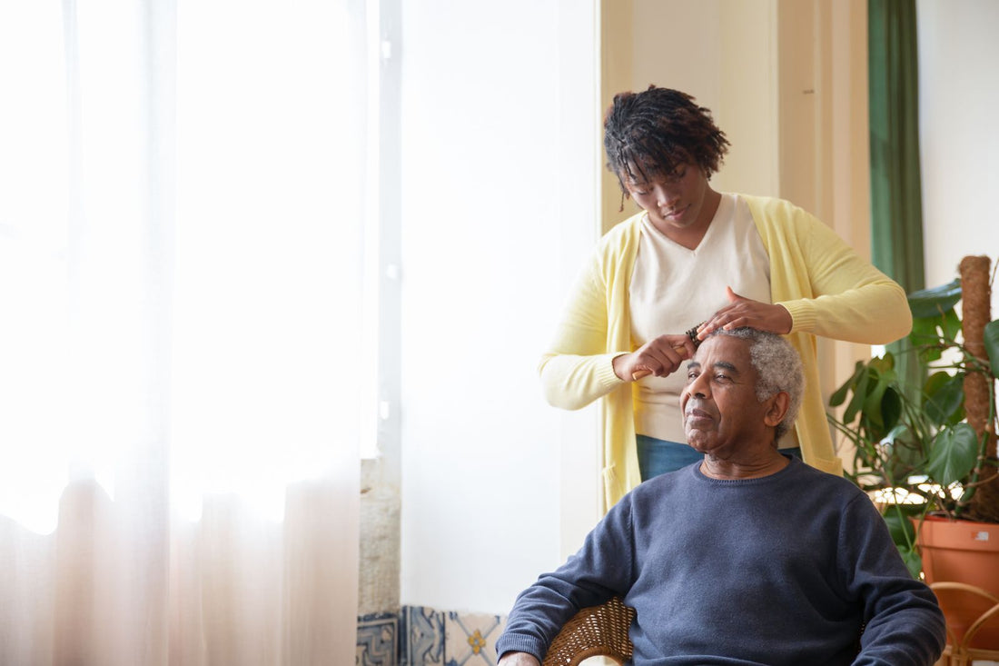 A caregiver gently combing an older man's hair by a bright window at home