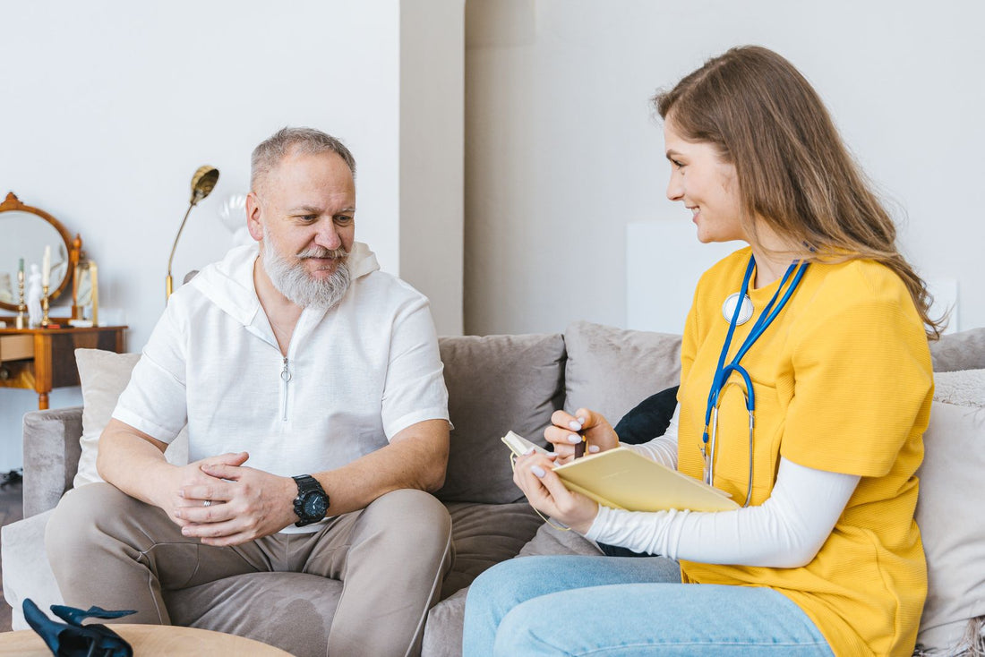 A smiling home-care nurse consulting with an older man on his couch